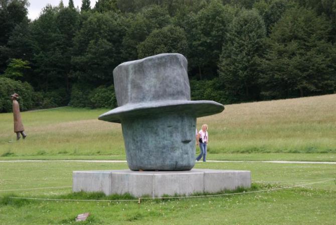 芝生の中に展示されている、シルクハットをかぶった人物の巨大な彫刻の作品の写真