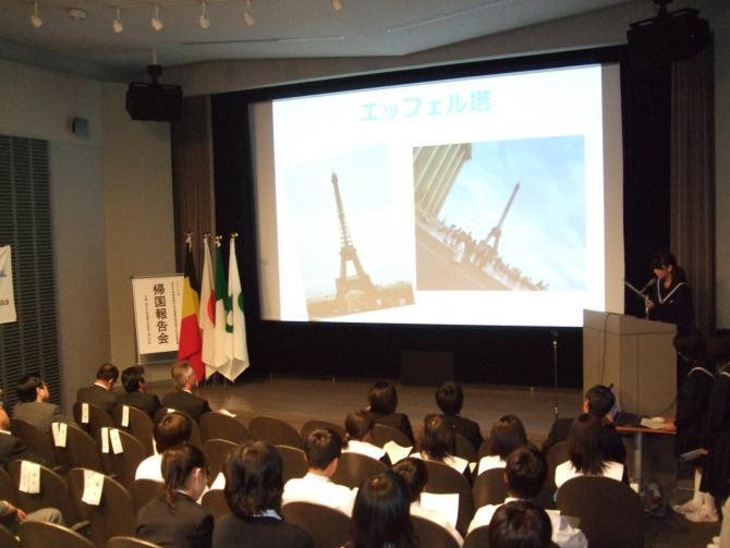 前方のスクリーンに映し出されたエッフェル塔の映像と発表を聞いている生徒たちの写真