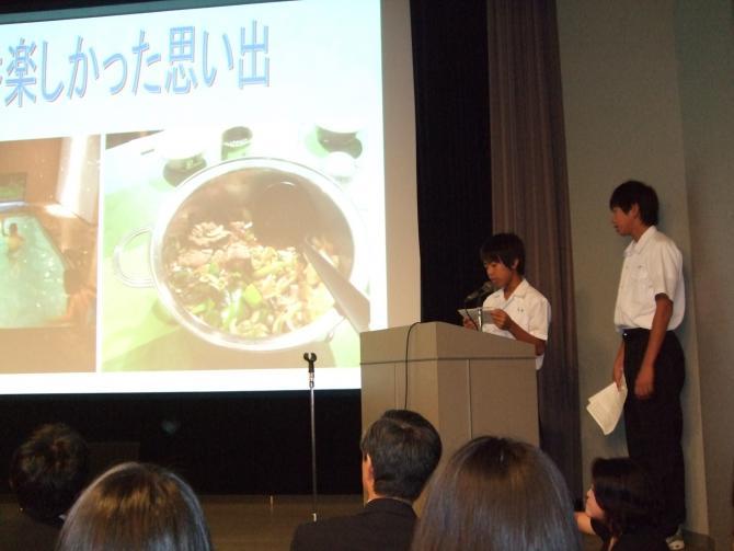 スクリーン横の演壇に立って発表をしている2人の男子生徒の写真