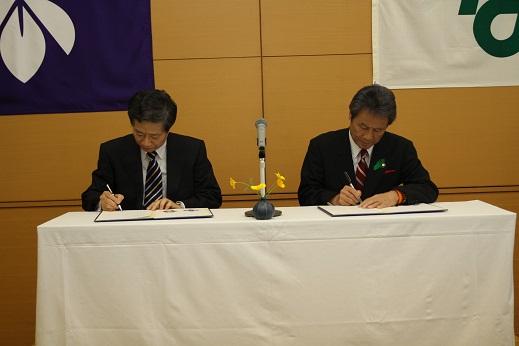 高島忠義学長と市長が協定書にサインをしている写真