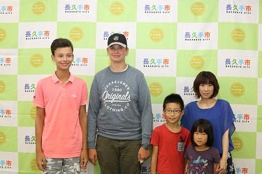 ピンク色のポロシャツを着た男の子と黒い帽子を被った男の子とホストファミリー親子(お母さん、男の子、女の子の兄弟)で写っている写真