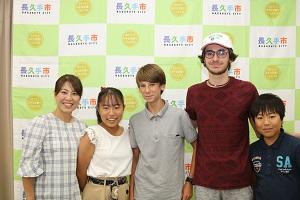 グレーのポロシャツを着た男の子、白い帽子の男性、ホストファミリーの親子(お母さん、お姉ちゃん、弟)が笑顔で写っている写真