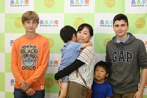 オレンジ色のティーシャツを着た男の子、グレーののトレーナーを着た男の子の間にホストファミリーの親子(お母さんに抱っこされている弟、と青いティーシャツを着たお兄ちゃん)が移っている写真