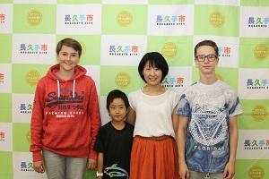 赤いトレーナーを着た女の子と黒ぶち眼鏡をかけた男の子とホストファミリーの親子(お母さんと黒いティーシャツの男の子)が写っている写真