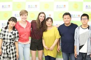 ピンク色のパーカーを着た女性と黒の短パンをはいた女性、ホストファミリーの親子(ご夫婦と男の子と女の子の兄弟)が笑顔で写っている写真