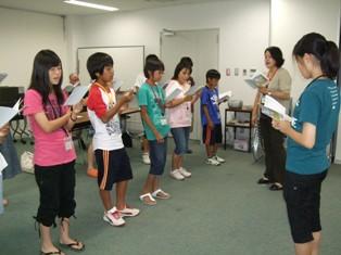 手に持った資料を見ながら並んで立っている生徒たちと女性教師の写真