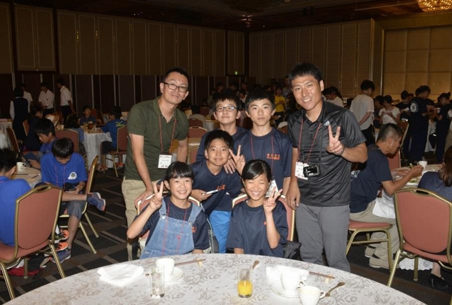 少年消防クラブ交流会の会食会場でスタッフとキッズ団員が記念撮影している写真