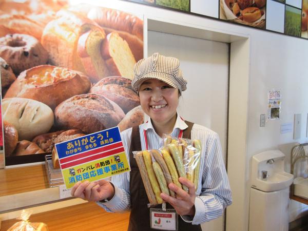 長久手温泉 あぐりん村のスタッフが左手にパンを、右手に消防団応援事業所表示証を持って写っている写真