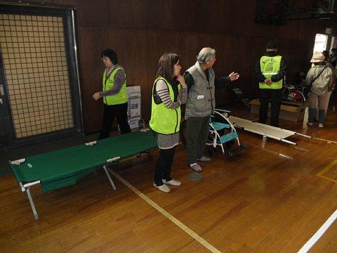 緑色の簡易ベッドを展示しているブースの前に女性スタッフと男性が立って話しをしている写真