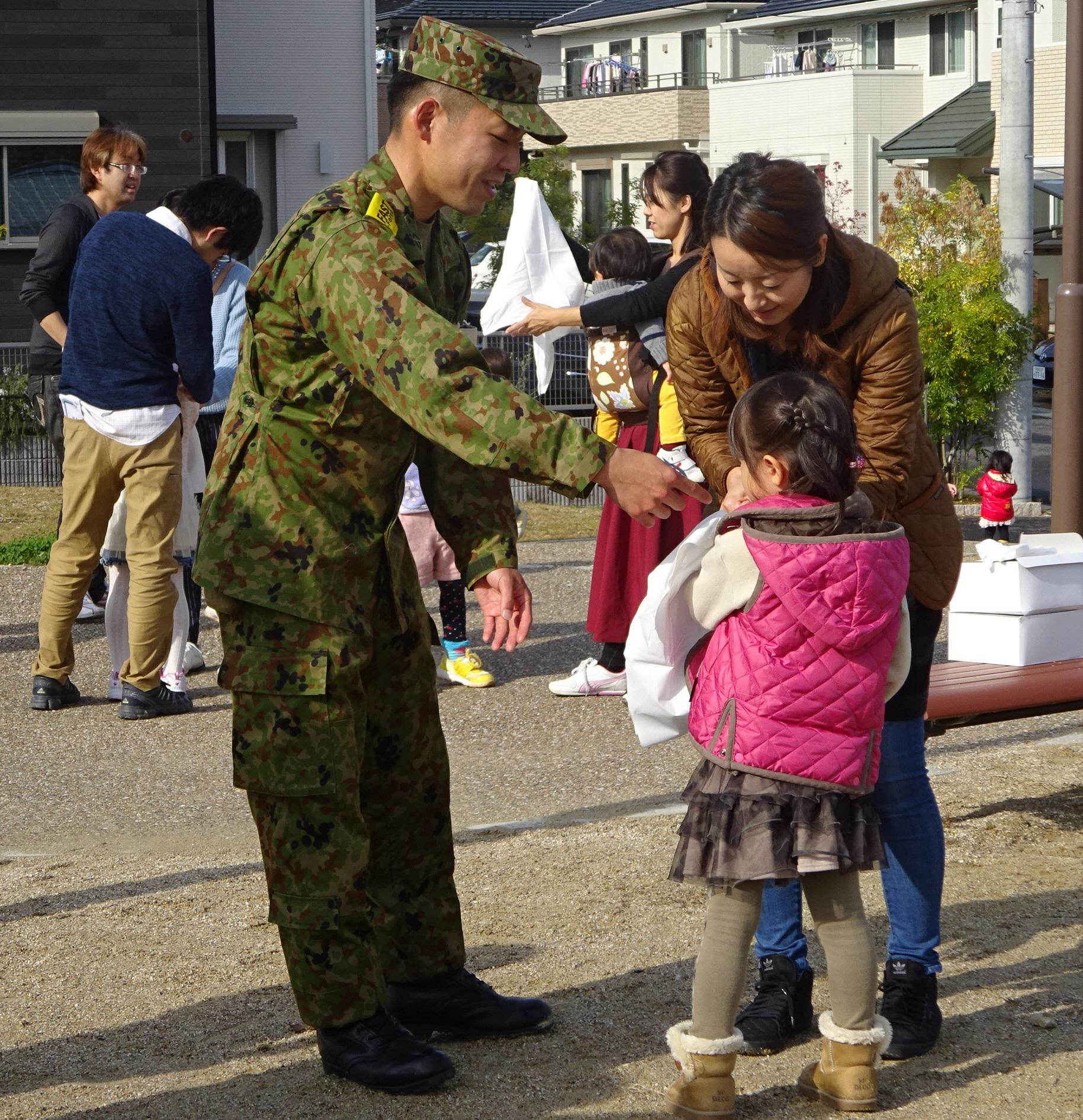 自衛隊員の指導の下、子供に三角巾を結ぶ母親の写真