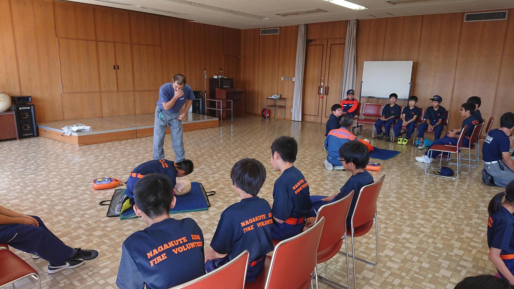 救命講習でマネキンに話しかけている男子の様子を講師や同じグループのメンバーが見ている写真