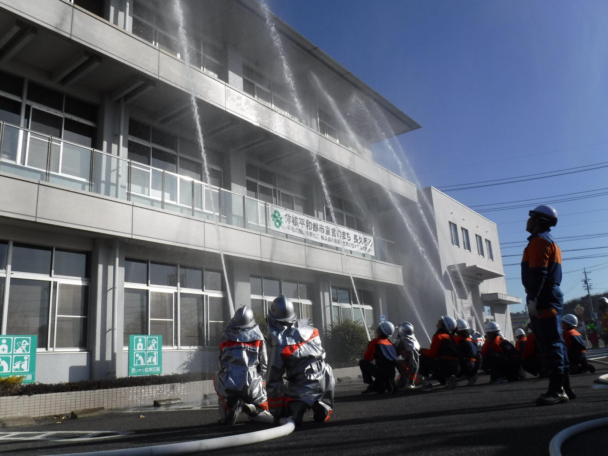 消防団員たちが建物に向かって放水している写真