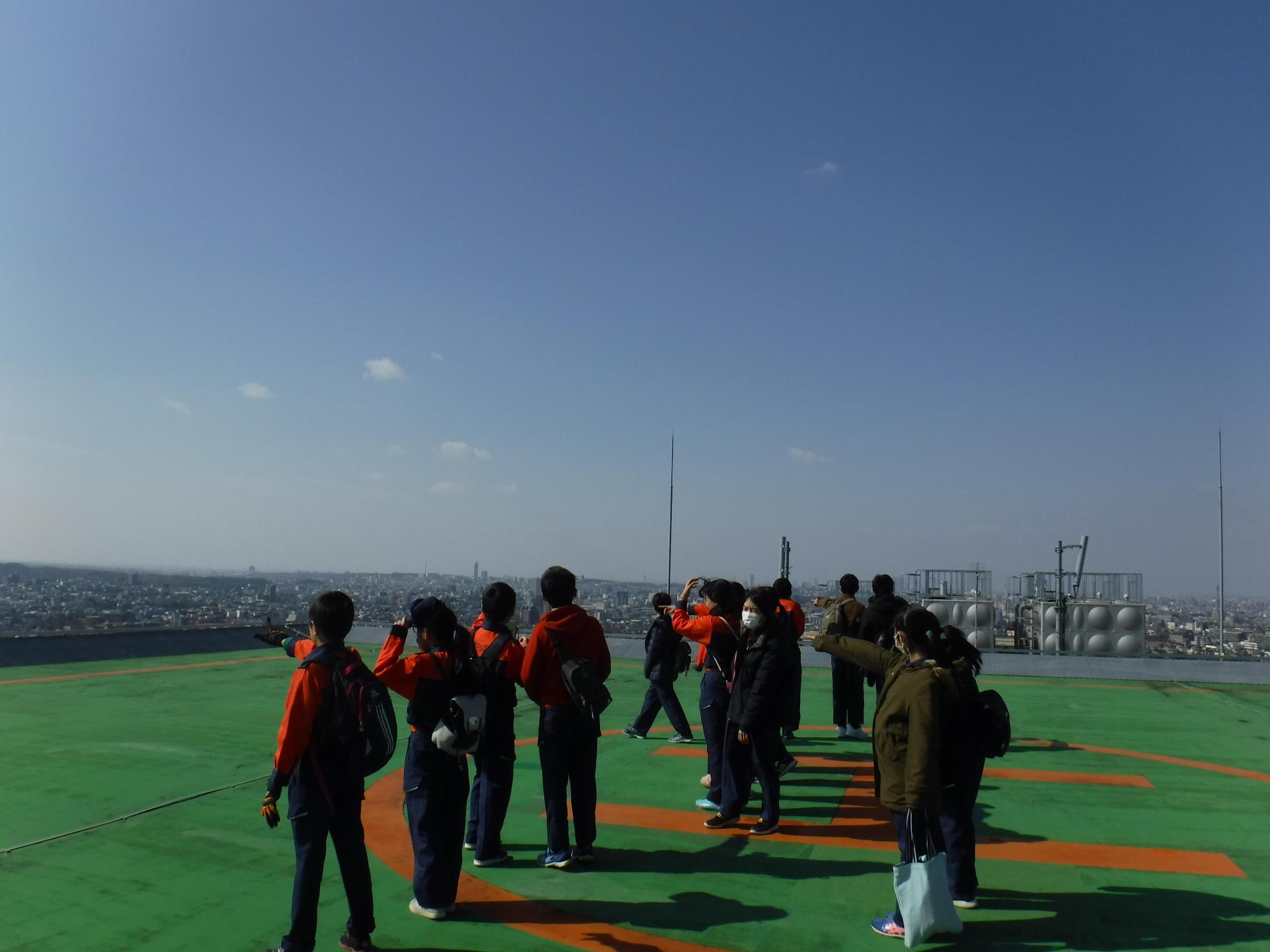 屋上ヘリポートの真ん中で何かを指さしている長久手市キッズ消防団の写真
