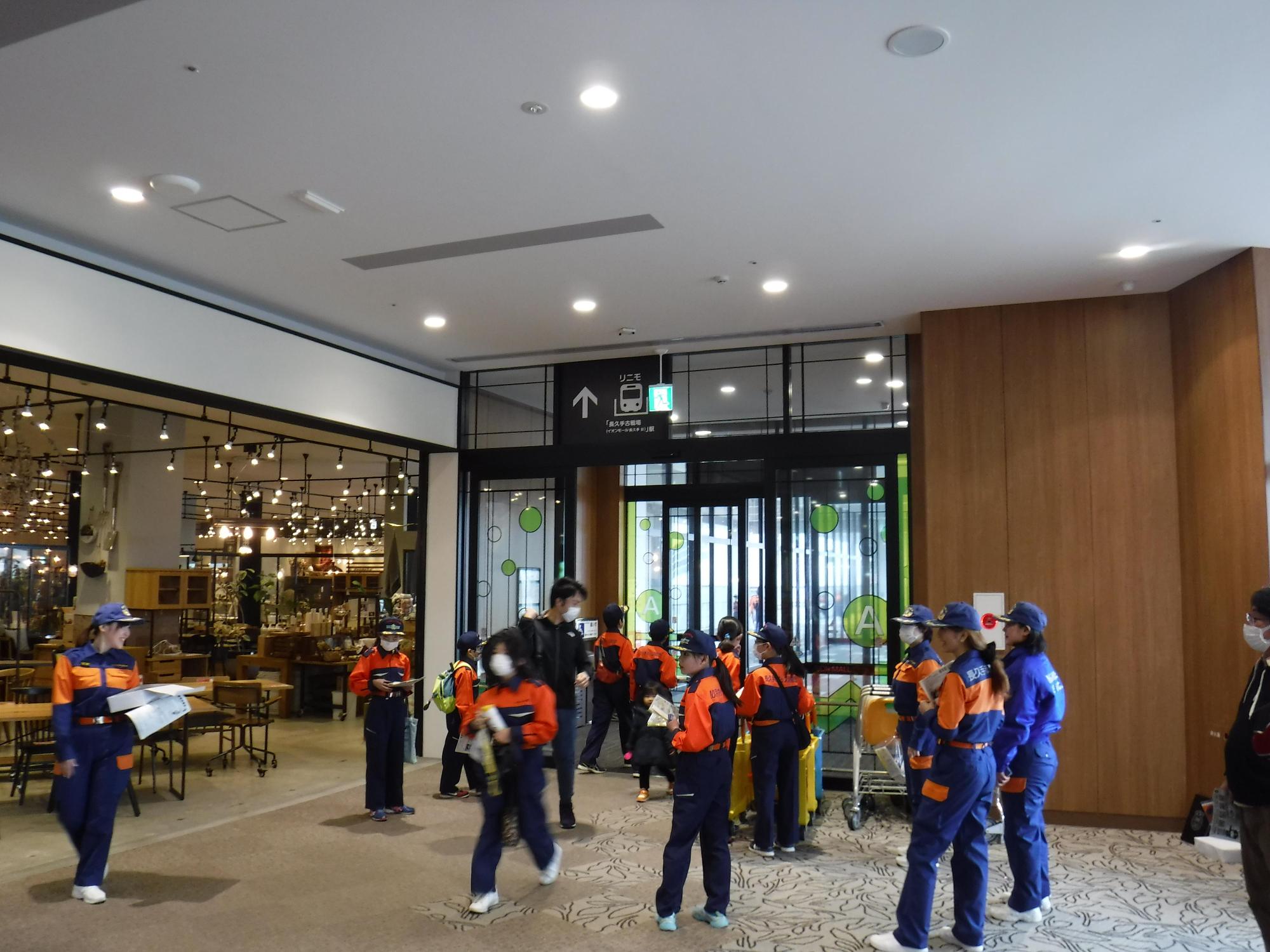 女性消防団(ポピーズ)と消防団の格好をした子供たちがモールの入り口付近で広報活動を行っている写真