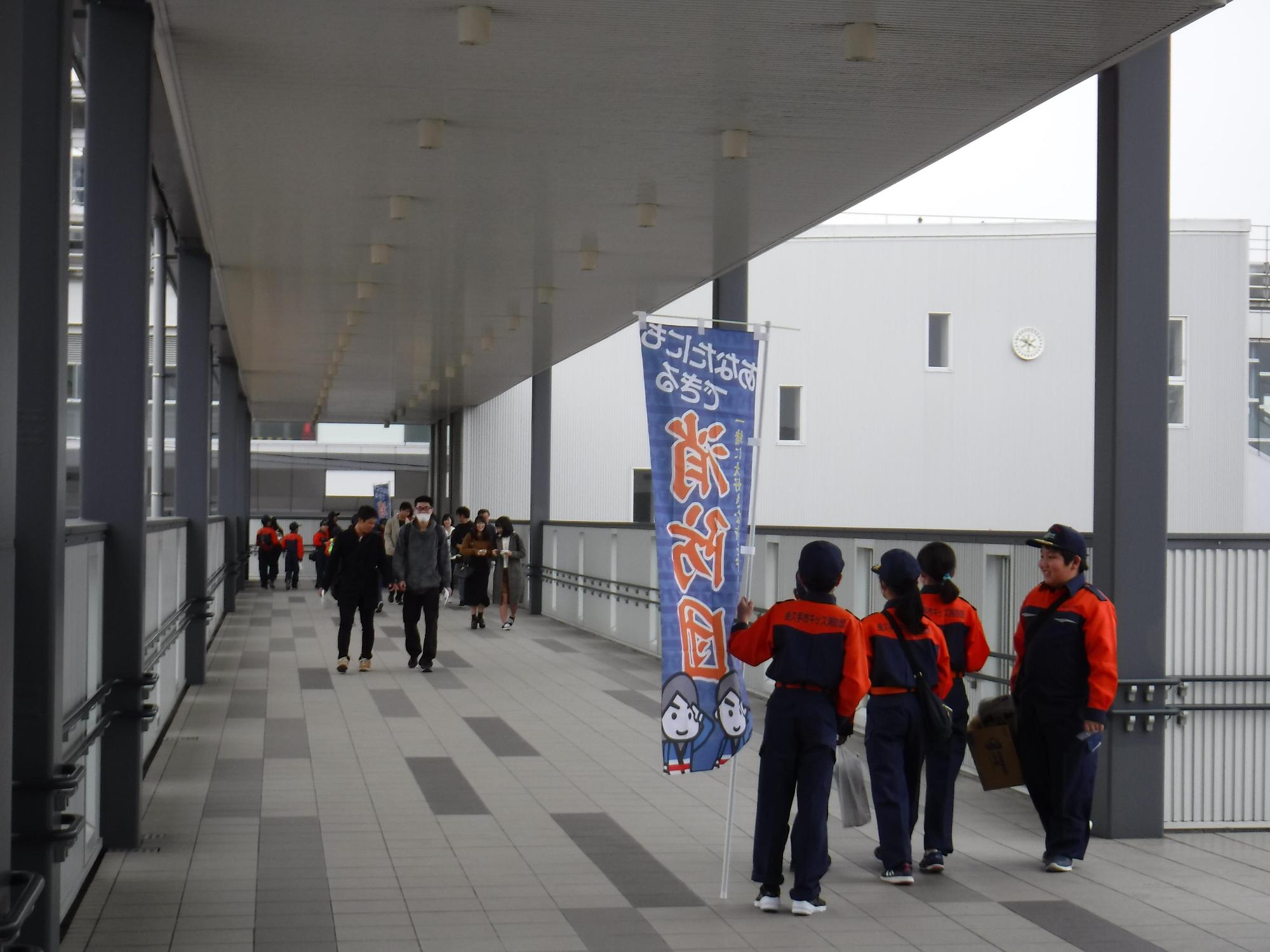 消防団の格好をした参加者が「あなたにもできる消防団」と書かれたのぼりを持って広報活動をしている写真