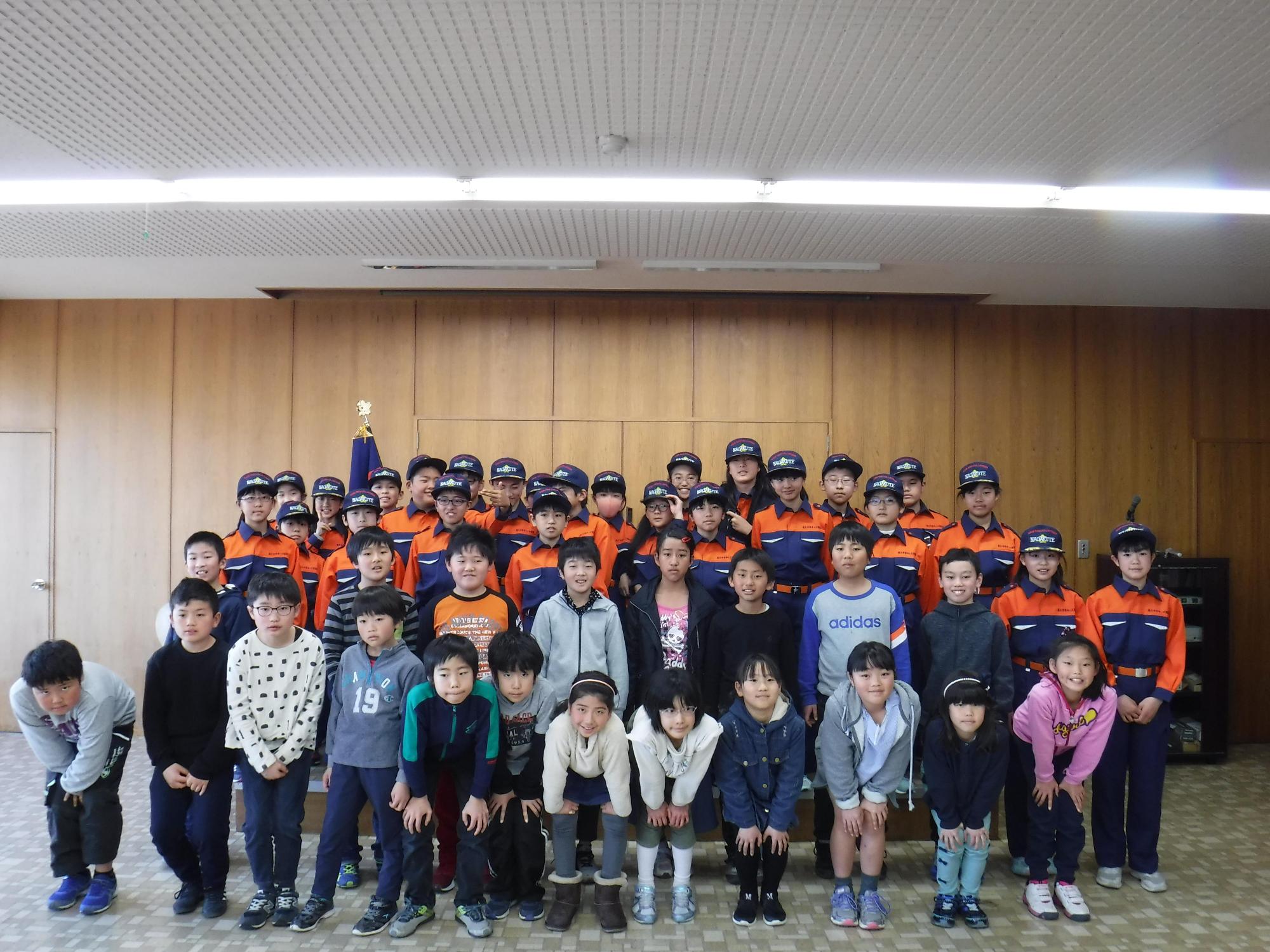 入団した私服姿の子供たちの後ろに消防団の制服姿の長久手市キッズ消防団たちが並んで記念撮影している写真