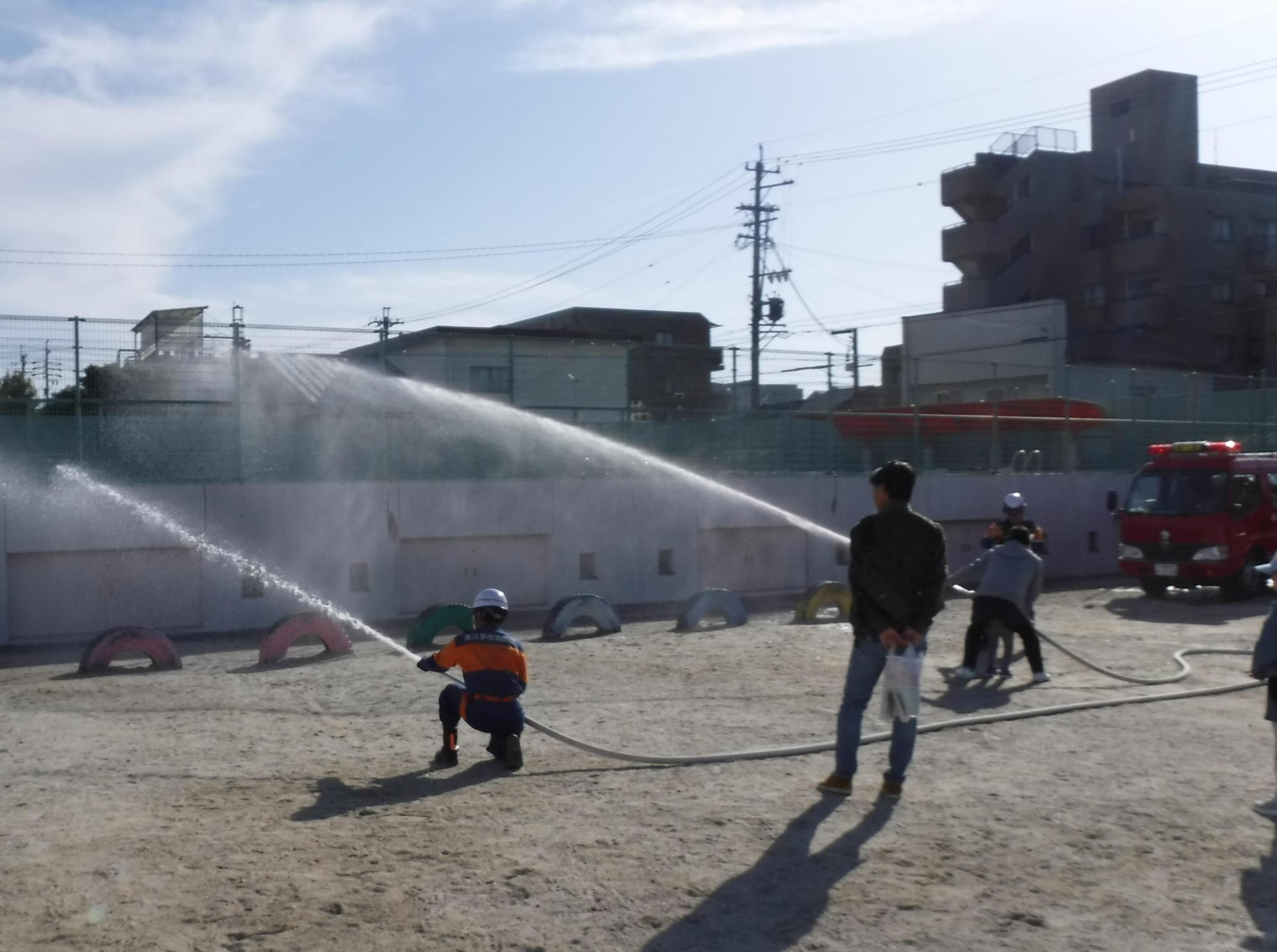 長久手市消防団の団員と一緒に放水体験をしている参加者の写真