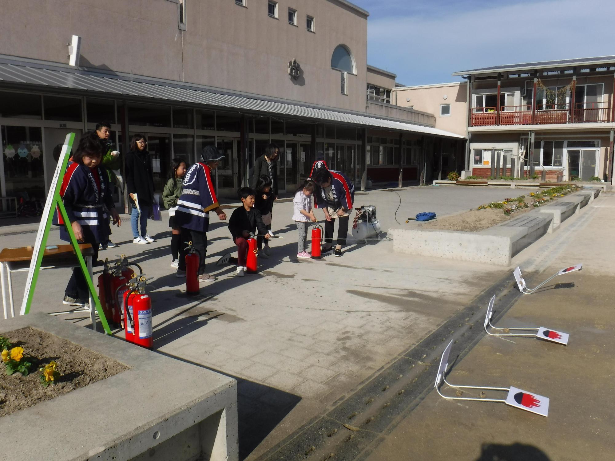 法被姿の長久手市女性消防クラブのスタッフと一緒に消火器の放射をする参加者親子たちの写真