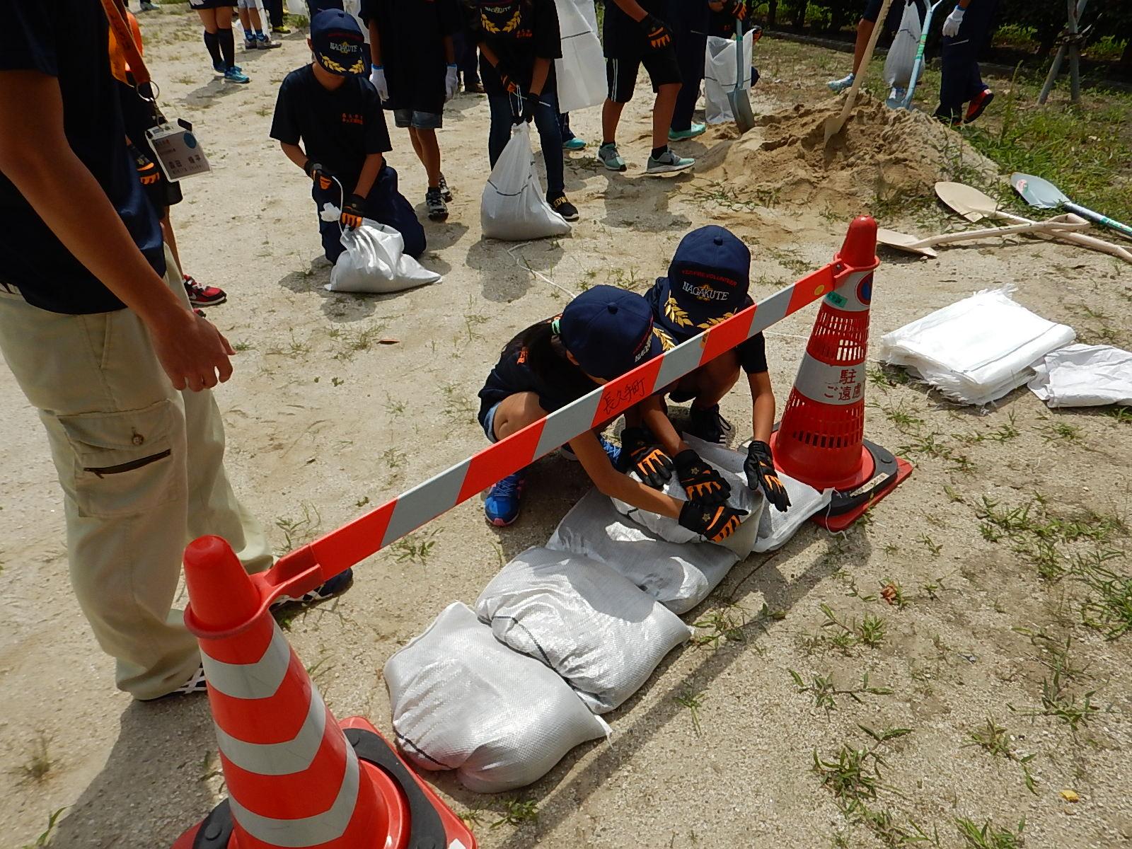 工事用コーンと工事用コーンの間に土のうを並べるキッズ消防団員たちの写真