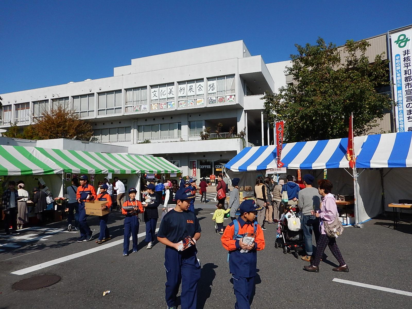 キッズ団員たちがテントの出店の前を消防団員募集のポケットティッシュを持って歩いたり、防火広報をしている写真