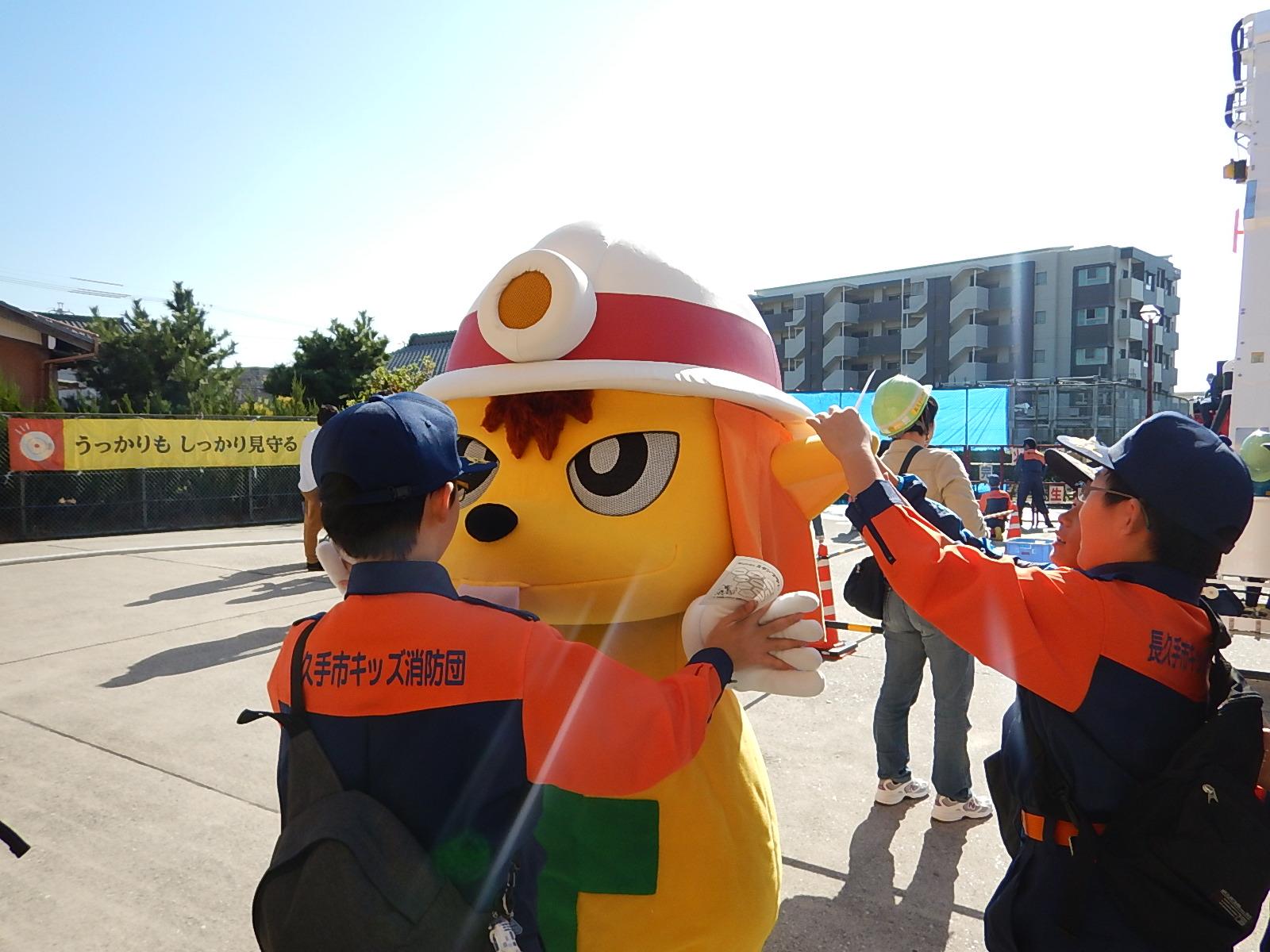 消防士のゆるキャラとハイタッチをするキッズ消防団員の写真