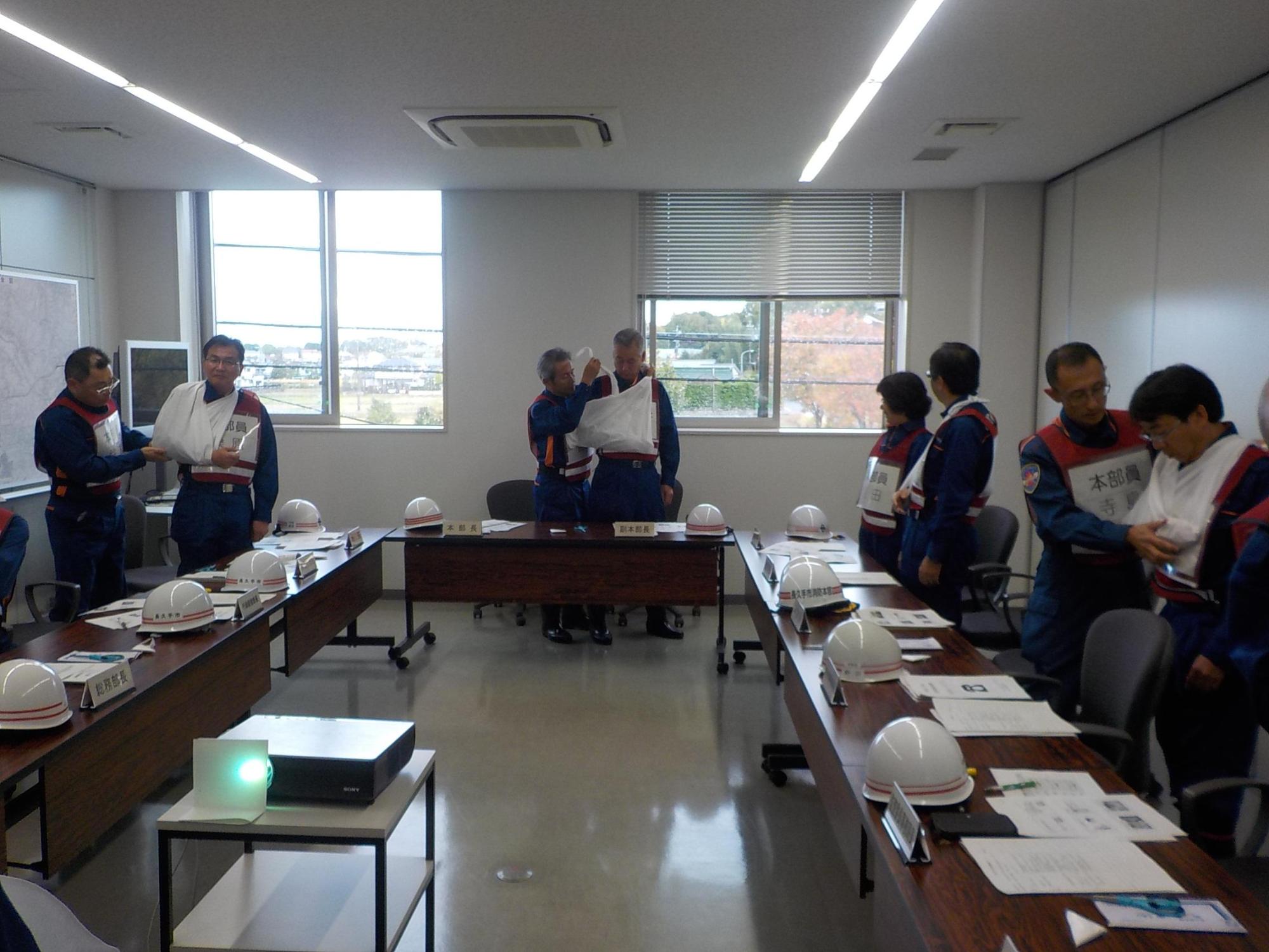 対策本部員が2人1組になって三角巾結びの訓練を行っている写真