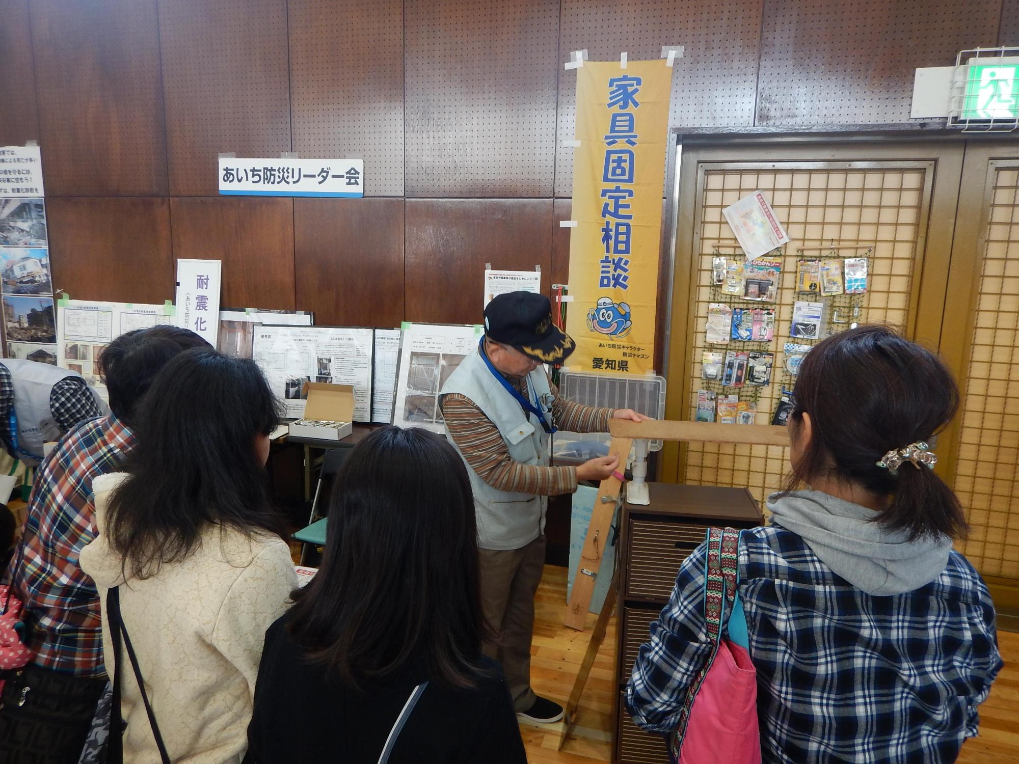 あいち防災リーダー会のブースに家具転倒防止啓発のパネルやグッズが展示されており、人が集まっている写真