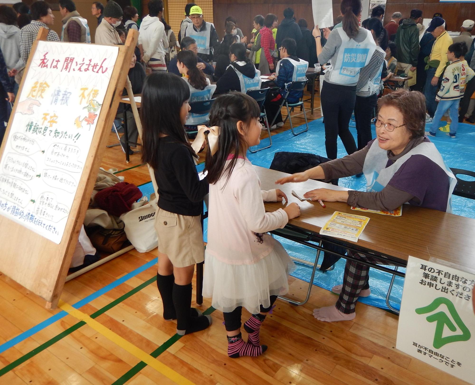 手話サークルの受付に座っている女性スタッフと女の子たちが話をしている写真