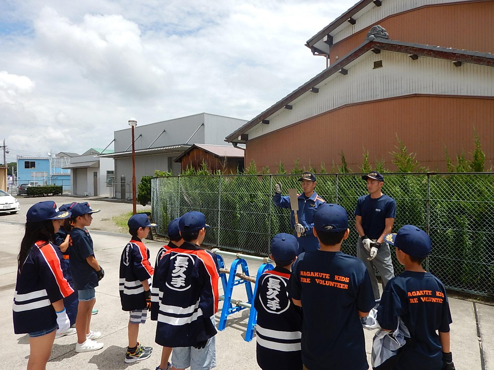 屋外でのこぎりを使い方について消防署員から説明を受けるキッズ消防団員たちの写真