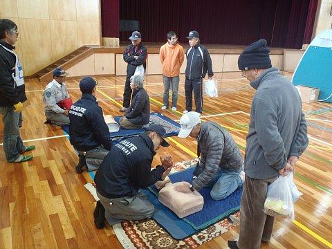 体育館の中で行われた、マネキンを使った心肺蘇生訓練を男性の消防職員から男性が教わっている写真