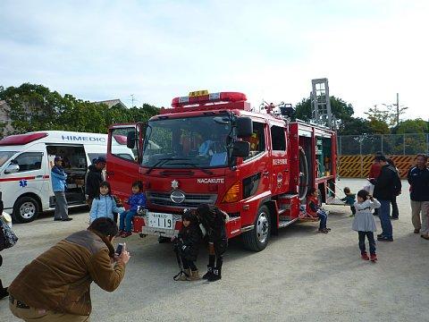 小学校の校庭に展示された消防車や救急車に乗ったり一緒に写真を撮ったりしている親子の写真