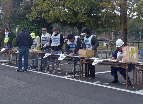 駐車場に長机を沢山繋げた受付で、男性が受付をしている写真