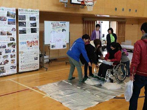 体育館の中の展示ブースの前で、女の子と母親がけん引式車いす補助装置体験をしている様子の写真
