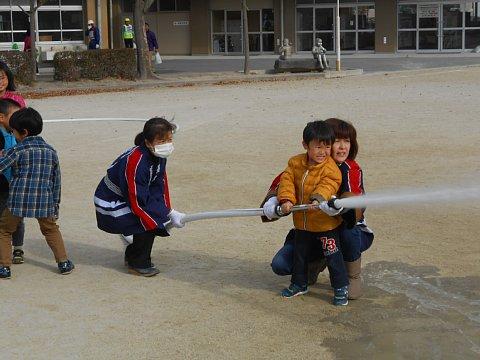 法被を着用した2名の女性が、放水訓練に参加した男の子のポンプを支えている写真