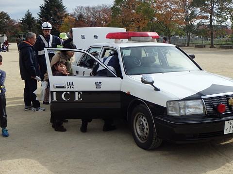 訓練に参加している親子や男性が、展示されているパトカーの中を見ている写真