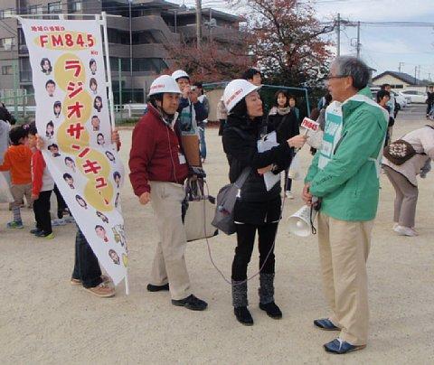 (長小)校庭にてラジオサンキューのスタッフからスピーカーを持っている男性にインタビューされている写真