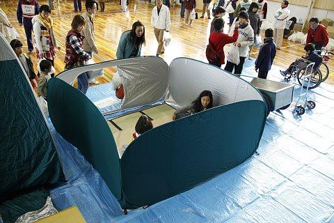 (長小)体育館に設置の間仕切りされた避難所体験をする子供たちの写真
