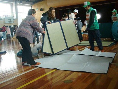(西小)体育館にて防災資機材の設営訓練で参加者が折り畳を床に敷いている写真