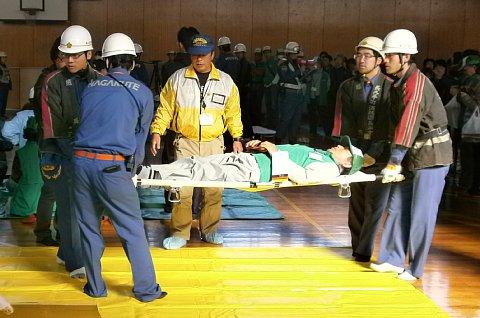 4名の男性消防団員が、担架に乗せられた男性を搬送する訓練を行っている写真