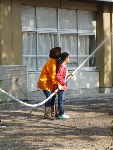 女の子がホースを持ち放水の訓練をしている後ろで女性スタッフが一緒にホースを持って支えている写真