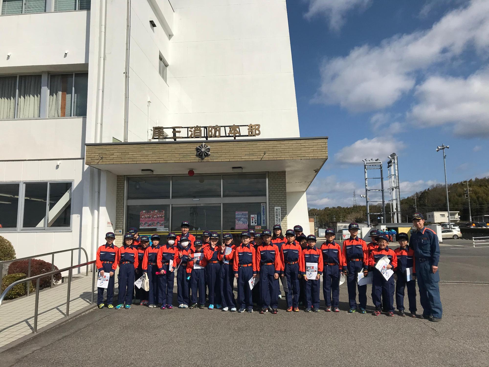 尾上消防本部の前で消防団員とキッズ団員たちが記念撮影している写真