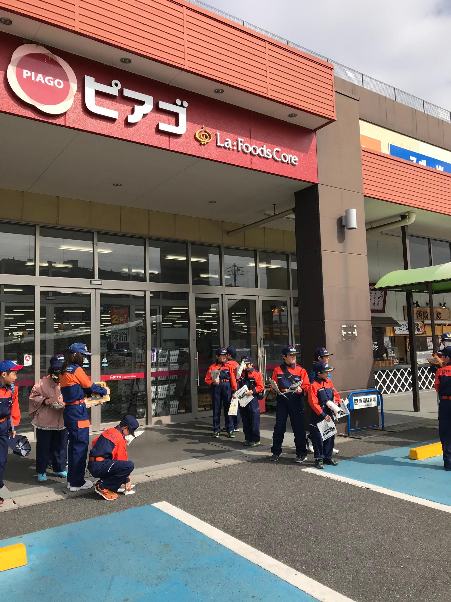 お店の入り口の両脇にキッズ消防団員たちが資料を持って立っている写真