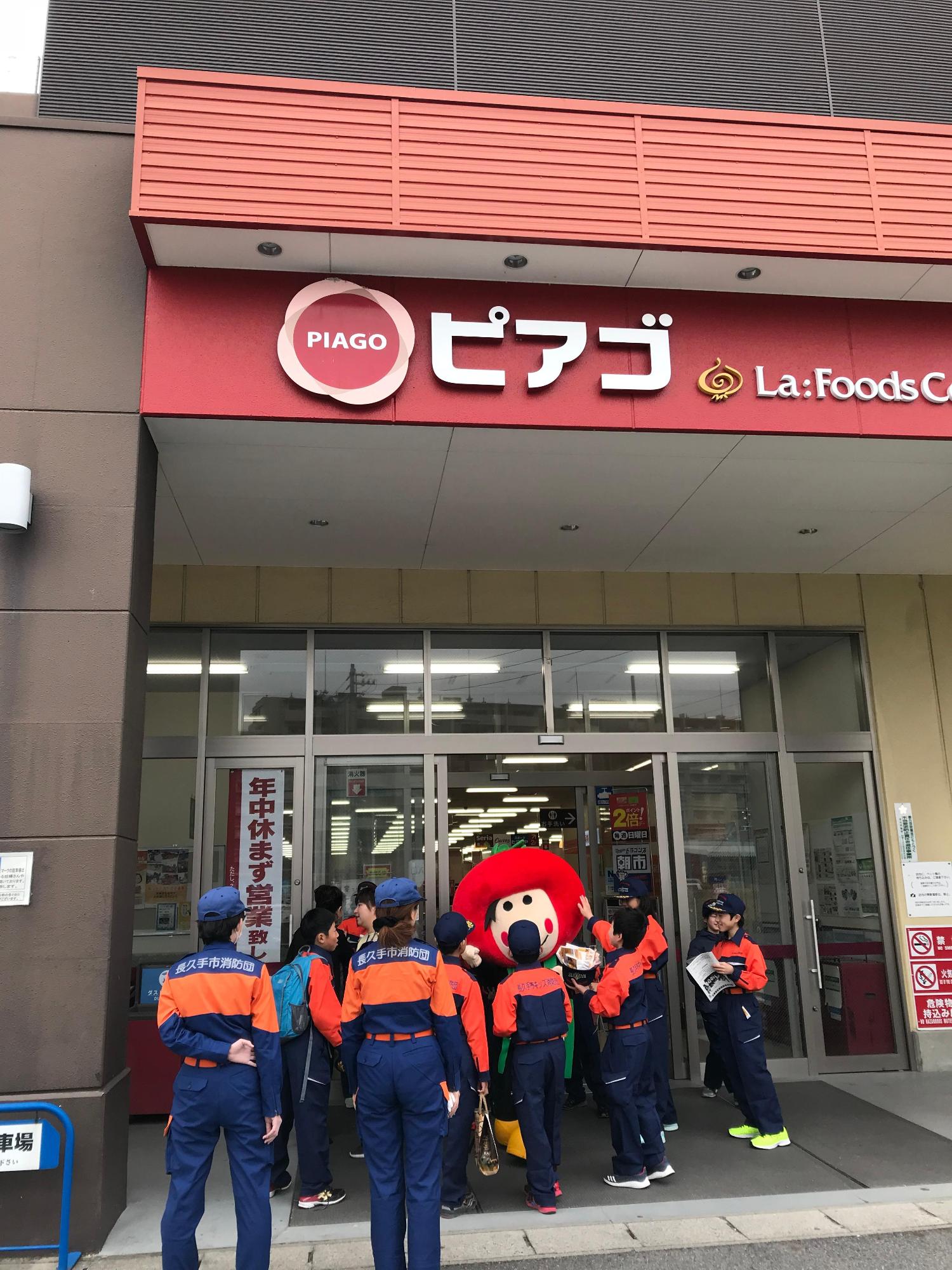 お店の入り口でトマトのようなゆるキャラをキッズ消防団員たちが触っている写真
