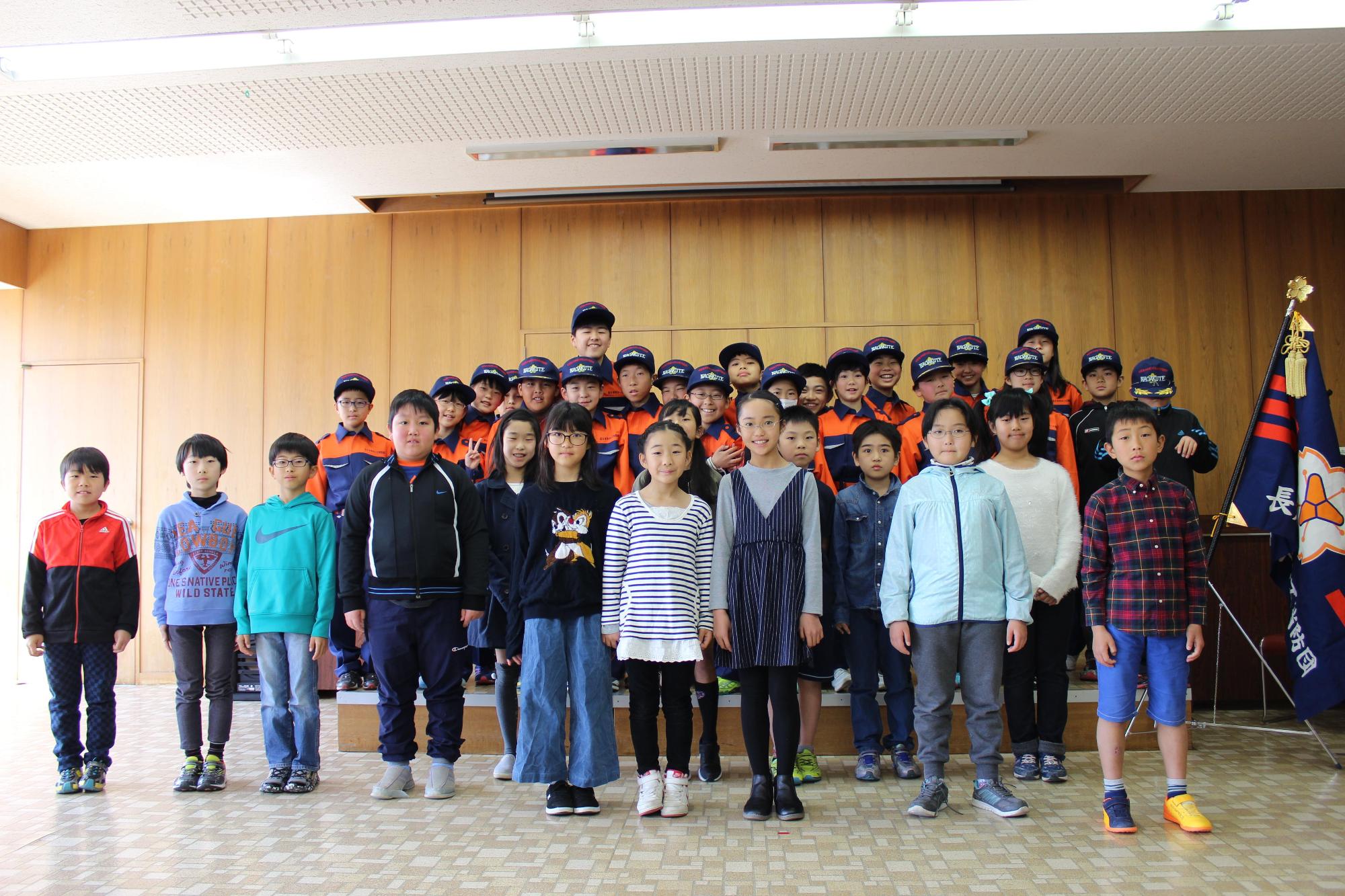 入団した私服姿の子供たちの後ろに消防団の制服姿の長久手市キッズ消防団たちが並んで記念撮影している写真