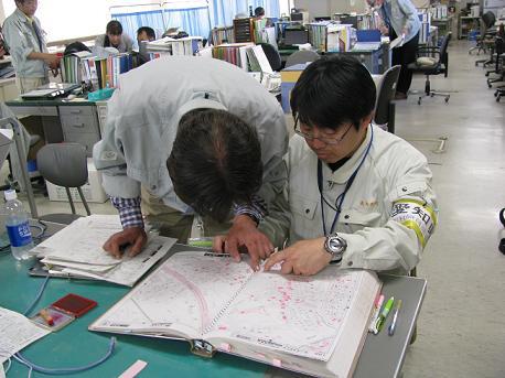 市の職員2名が机の上に地図を広げて、住所を調べている写真