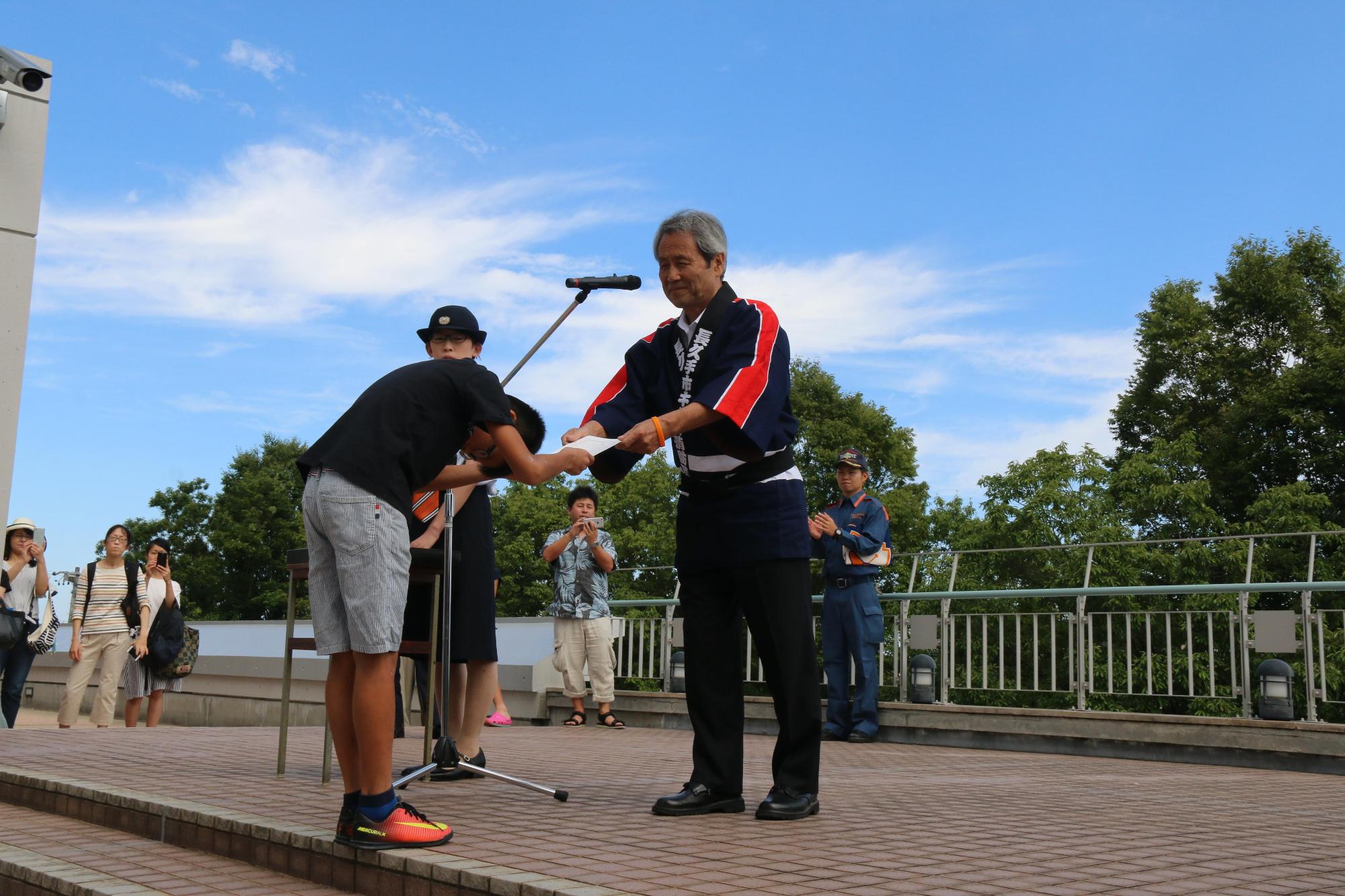 頭を下げながら両手で男の子が男性消防団から辞令を受け取っている写真