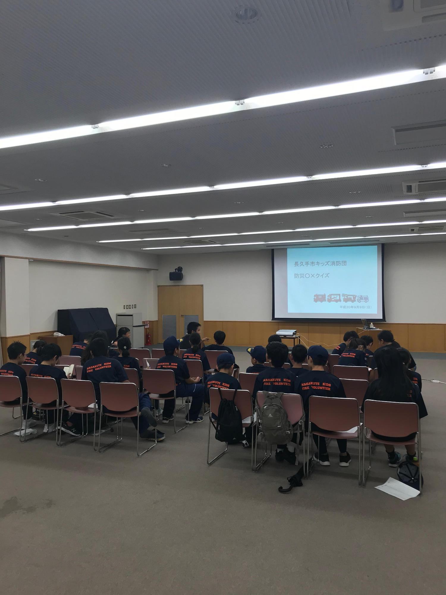 スクリーンに映し出された防災クイズで防災について学ぶキッズ団員たちの写真