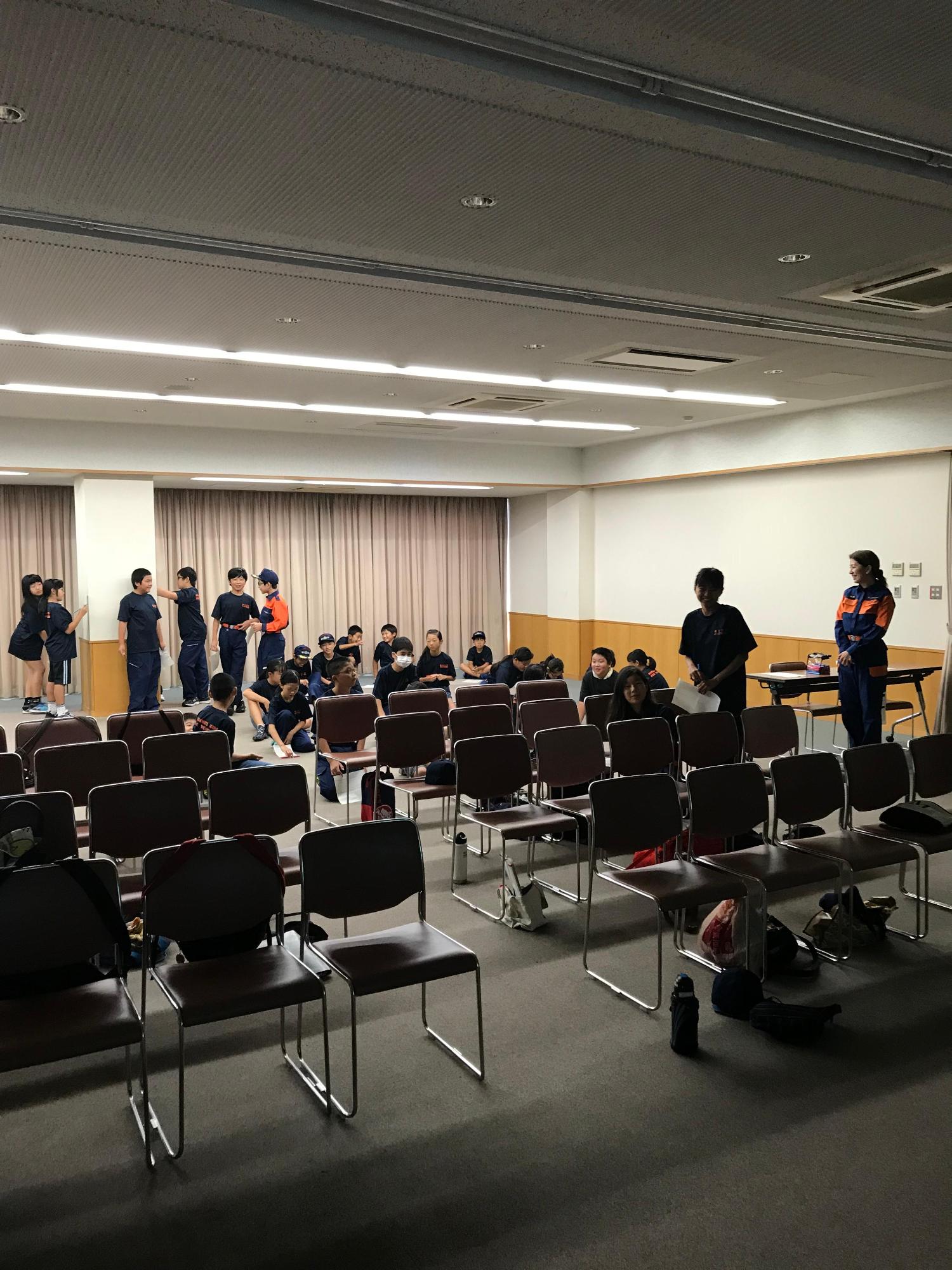 キッズ団員たちが並べられた椅子の後ろ方(灯りがついている方)で集まっている写真