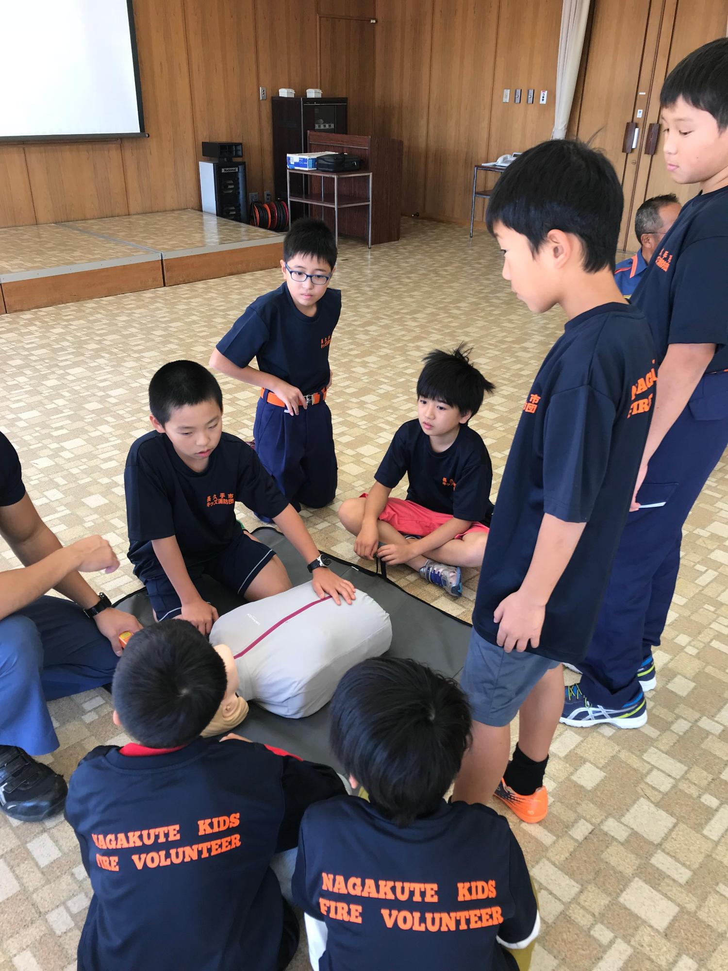 参加している子供たちが練習用の人形の周りに集まっている写真