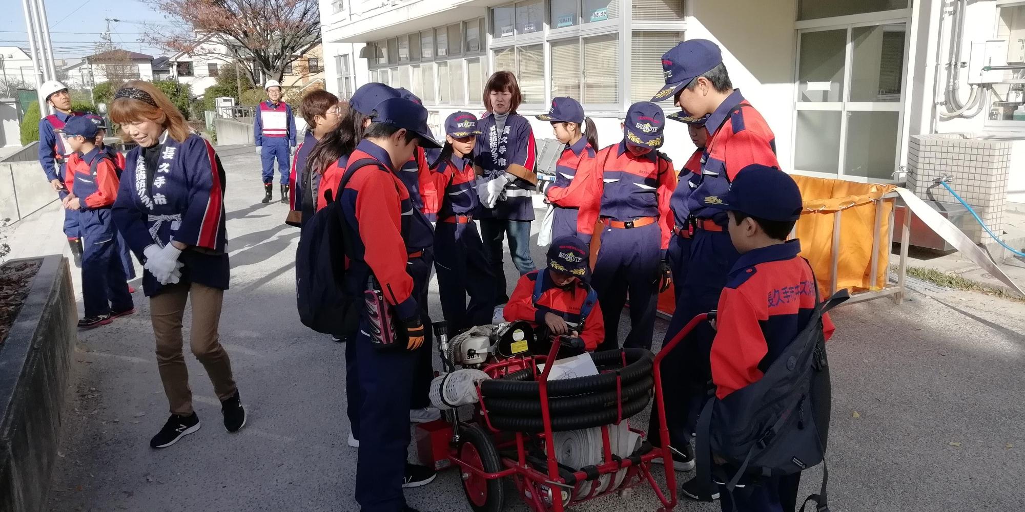 給水訓練用のホースの周りにキッズ消防団員たちが集まっている写真